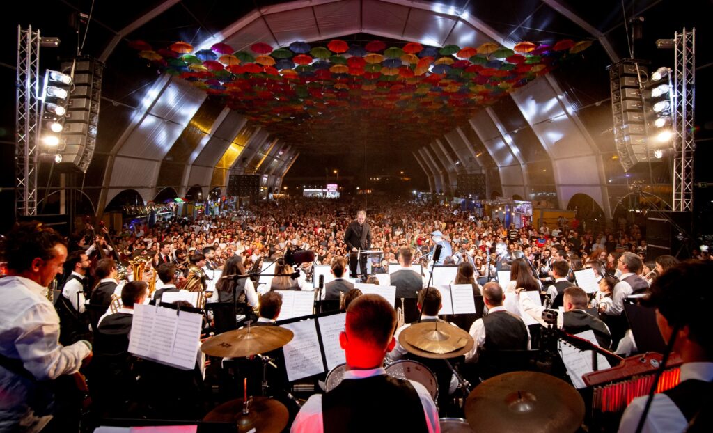 Photograph of a concert in an orbital igloo tent with alternating white and transparent tops, and of the main stage for the Agitágueda 2023 event.